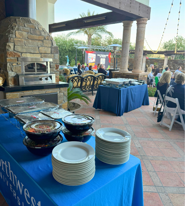 Corporate catering buffet station at an outdoor event with chafing dishes and plates.