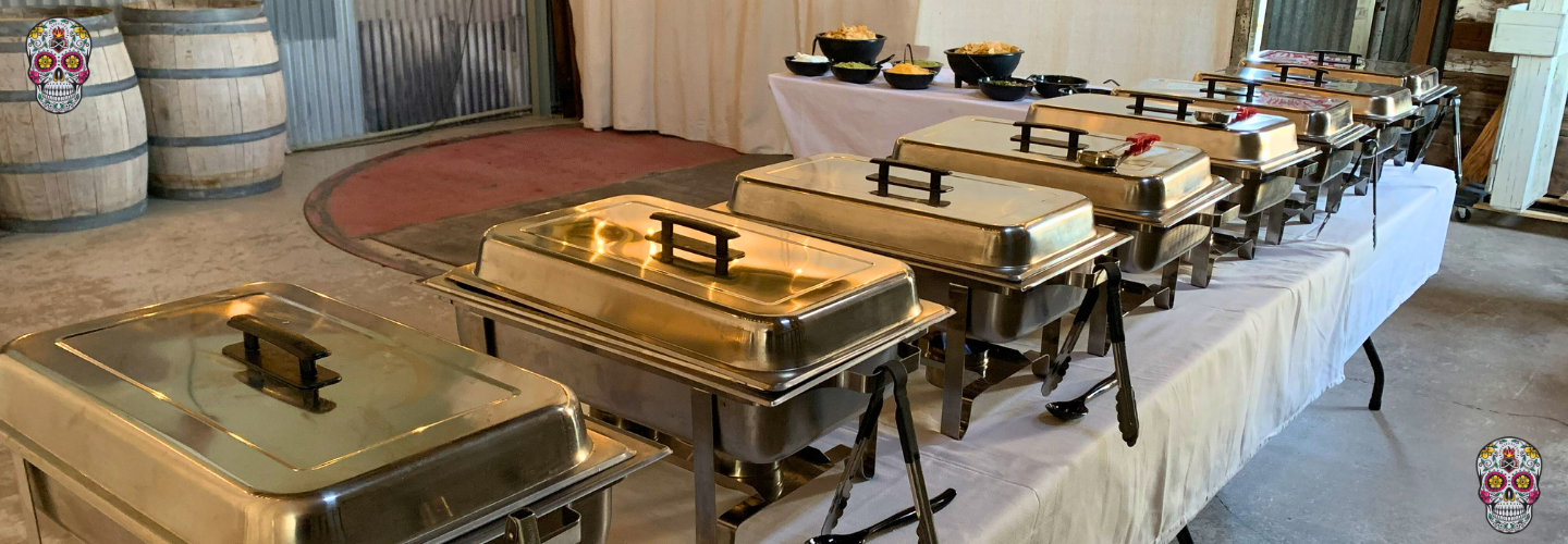 Corporate catering buffet with covered chafing dishes at a rustic event venue.