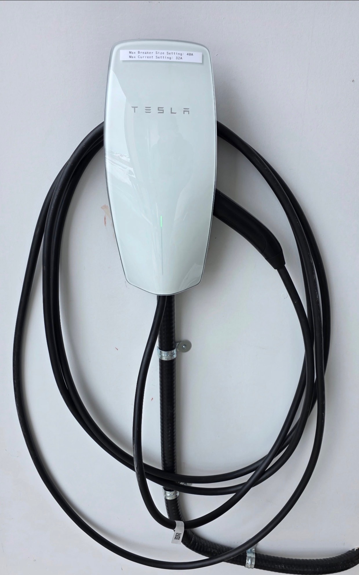 A Tesla Wall Connector installed against a white wall with safety label attached.