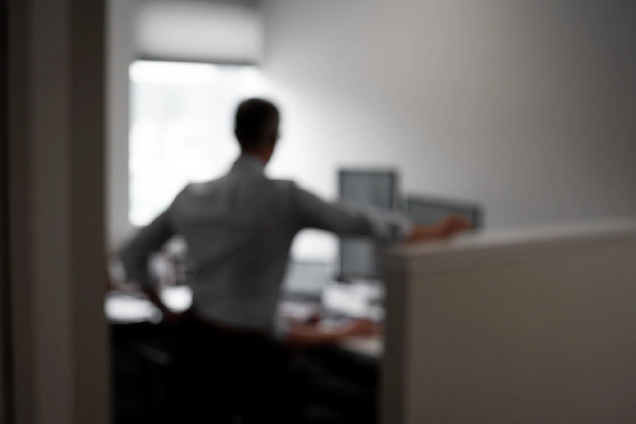 Blurred image of a person standing and leaning on a cubicle wall in an office setting.