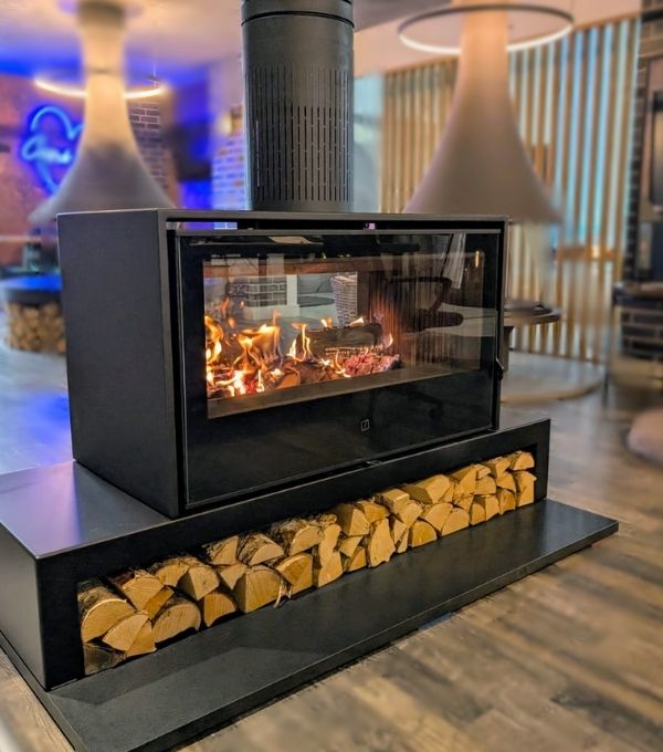 A side shot of the Axis double sided woodburning stove with a logstore below it