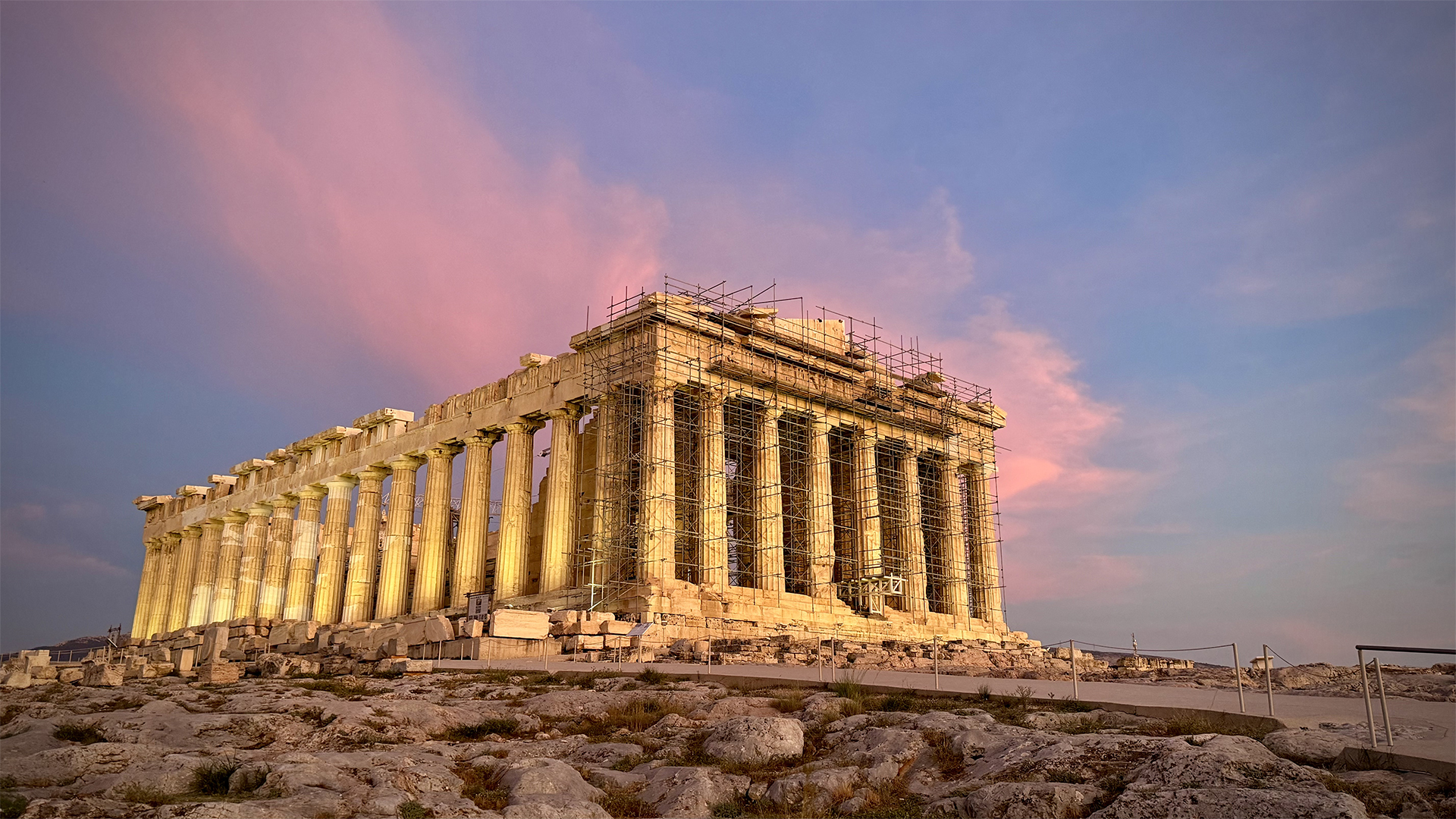 The parthenon with scaffolding, set against a pink-blue sky