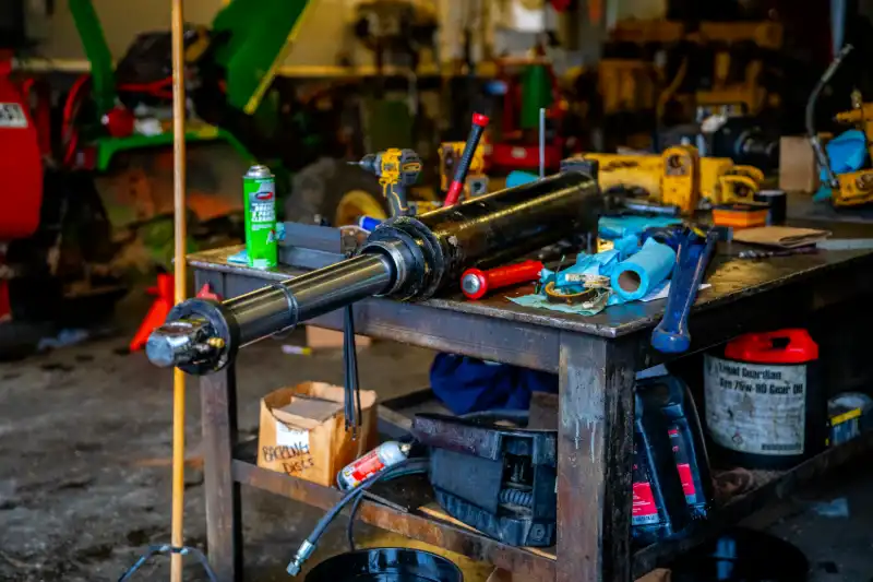 Hydraulic hose secured with steel worm-drive clamp amid dusty loader linkage, illustrating maintenance inspection focus.
