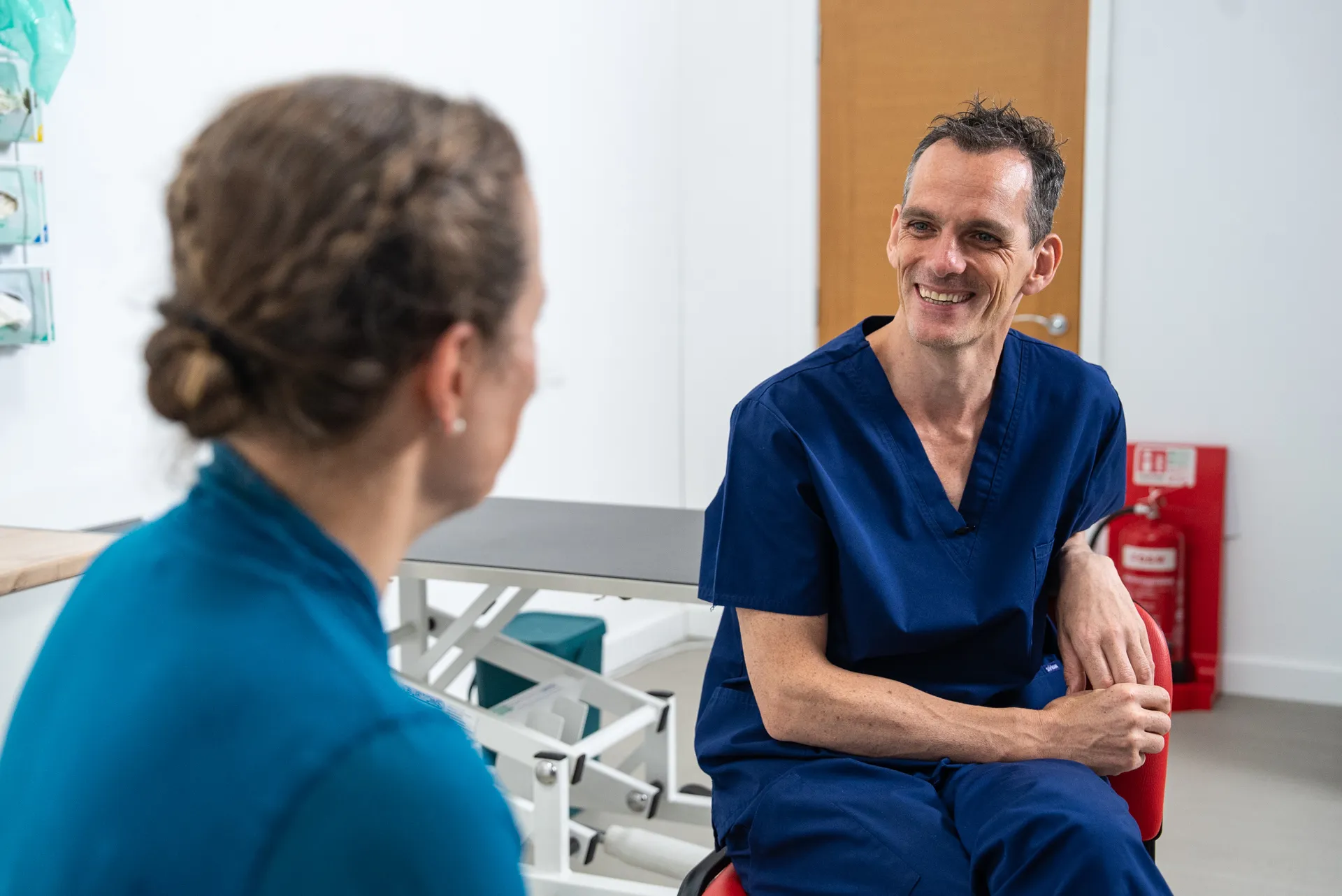 A man in scrubs sitting next to a woman in a chair.