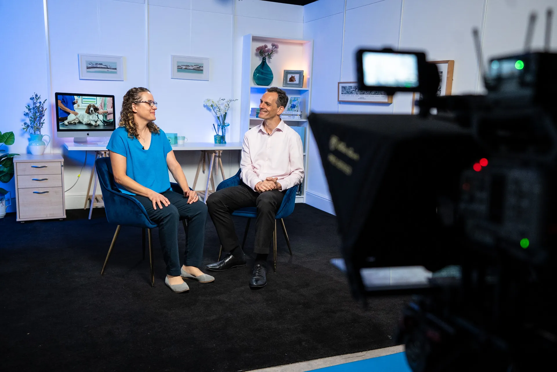 Man in white coat with yellow collar dipping a french fry into blue sauce filmed by a professional camera.