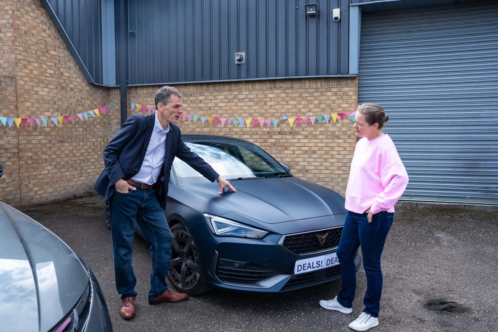 A man in a white shirt and a woman in a blue shirt sitting on blue chairs in a modern room with a bookshelf and a desk in the background.