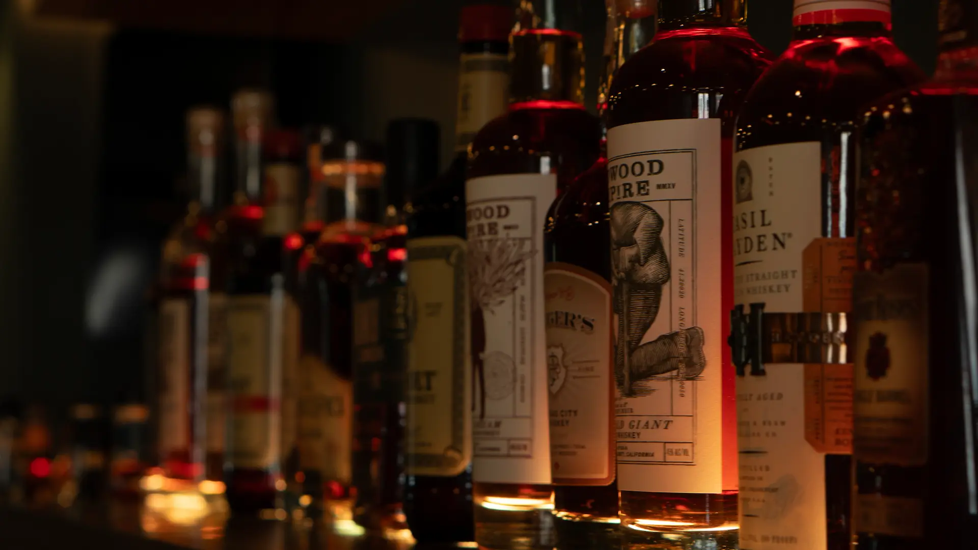 a dimly lit whiskey shelf, featuring high end and rare whiskies