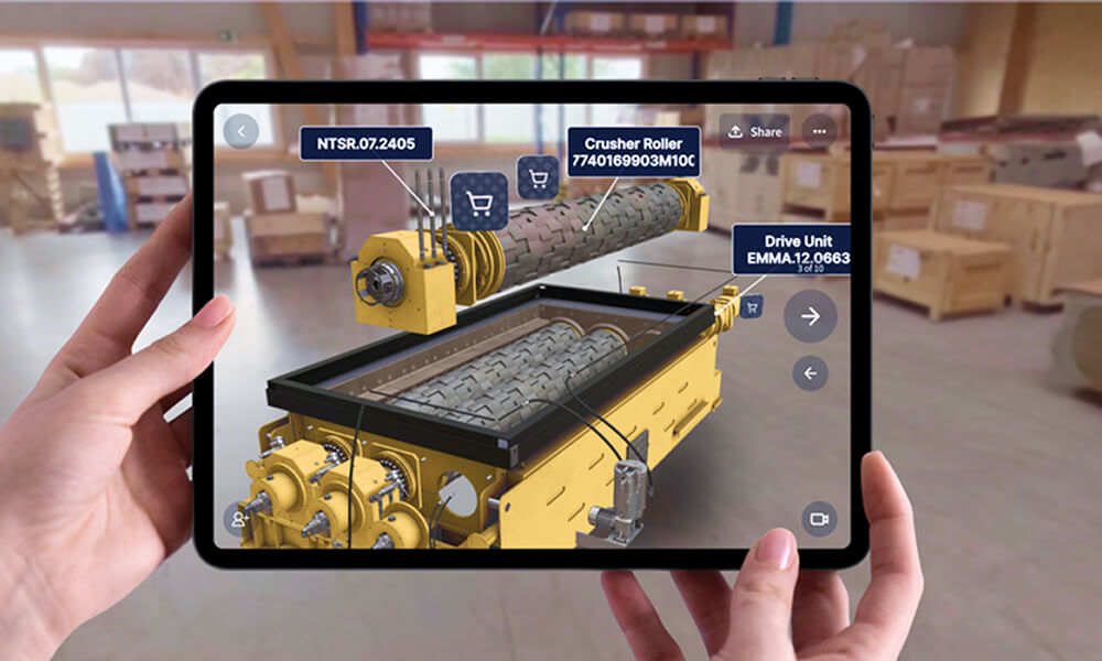 Hands holding a tablet displaying an augmented reality view of a yellow industrial machine with labeled parts: Crusher Roller, Drive Unit, and NTSR.07.2405.