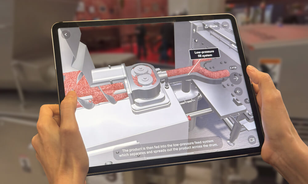 Hands holding a tablet displaying a 3D diagram of a low-pressure fill system in an industrial machine processing a product.