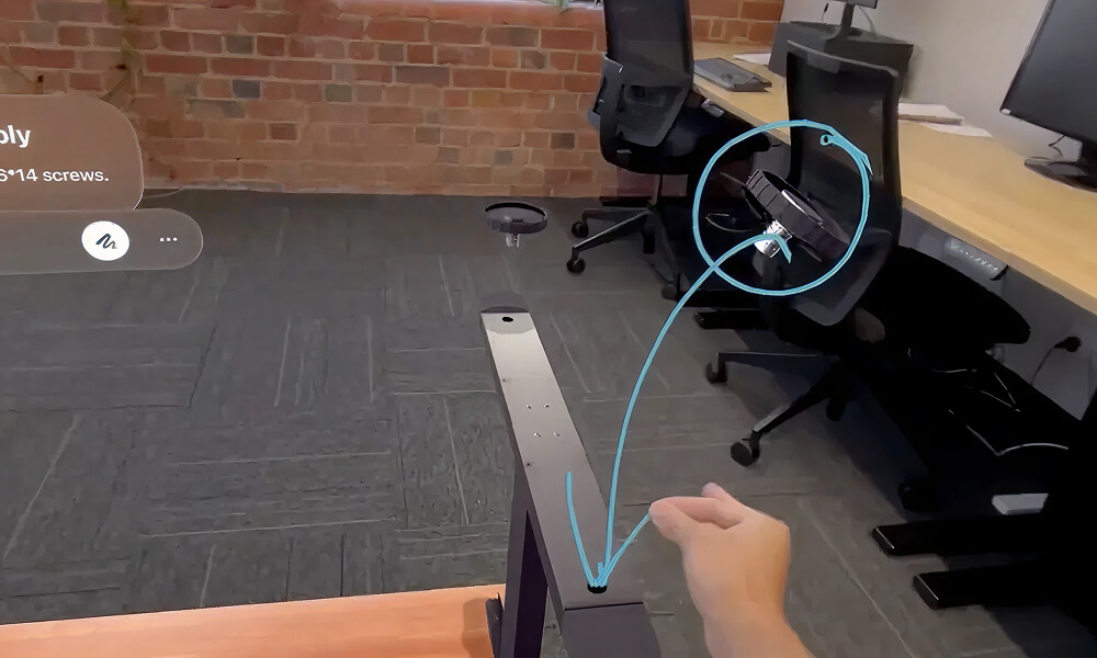 Hand installing a circular black component onto a metallic frame with a blue line indicating the placement, office chairs and desks in the background.