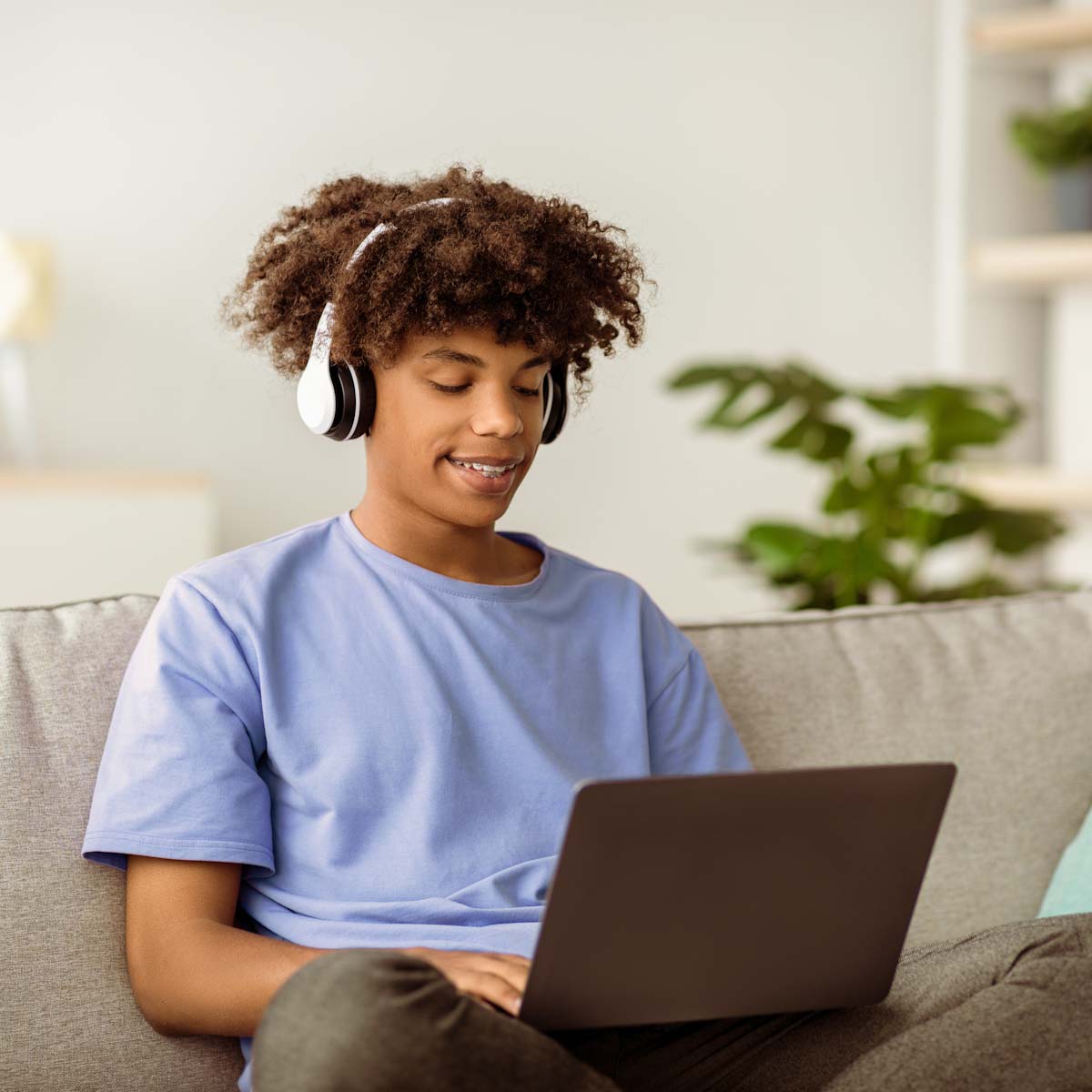 Teenager on laptop while sitting on couch wearing headphones