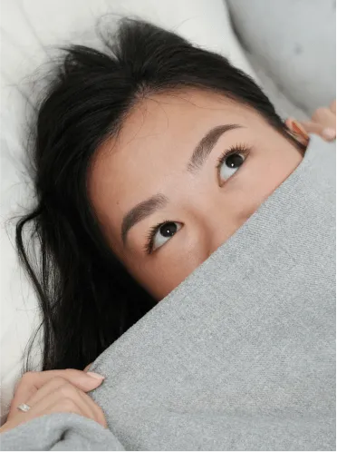A Singapoean girl covered up to half of her face under the bedsheets