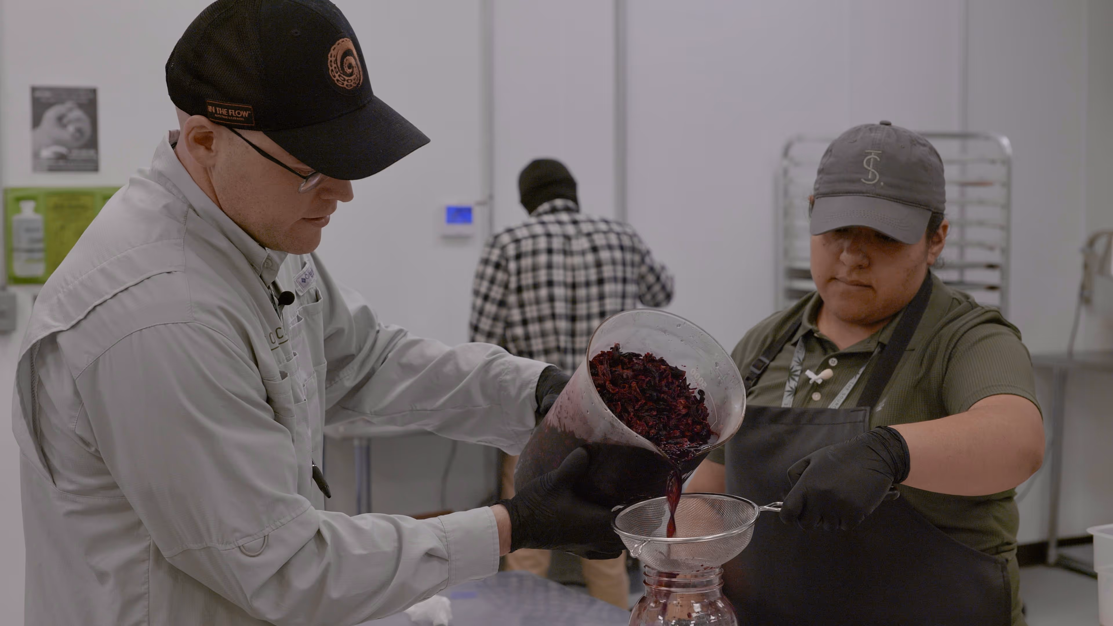 Retrato tomado dentro del laboratorio y cocina de The Source Craft Cannabis Company en Rogers, Arkansas. El retrato es de Yeci, Trevor, y Montana, El equipo de laboratorio y cocina de The Source. El equipo está usando batas blancas de laboratorio y equipo de protección personal, y se encuentran parados lado a lado en un laboratorio bien iluminado.