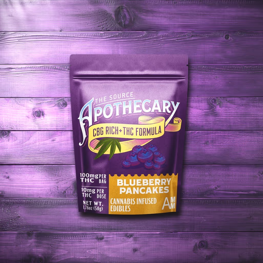 The Source Apothecary Cannabinoid Rich formula Blueberry Pancakes cannabis edibles are enriched with the alternative cannabinoid CBG plus THC. The indigo blue kraft paper packaging is shown from above and the background is multicolored wood.