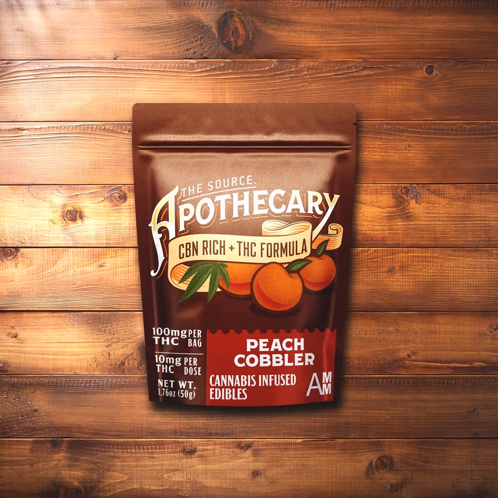 The Source Apothecary Cannabinoid Rich formula Peach Cobbler cannabis edibles are enriched with the alternative cannabinoid CBN plus THC. The brown and orange kraft paper packaging is shown from above and the background is multicolored wood.