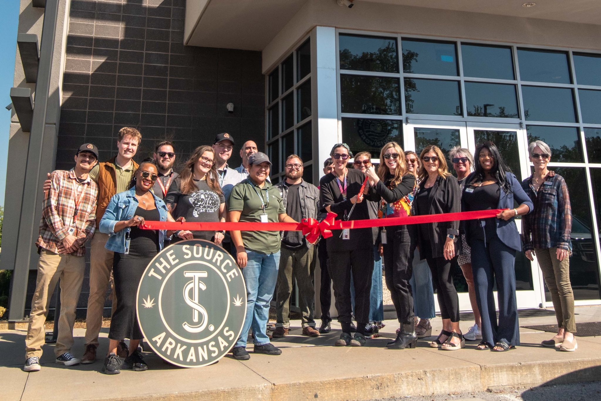 The Source Craft Cannabis team and Rogers Lowell Chamber of Commerce members cutting red ribbon at six-year anniversary celebration outside Rogers, Arkansas dispensary.
