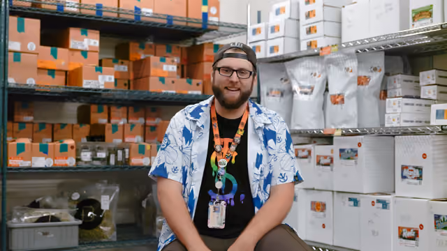 Zach in colorful shirt sitting in The Source's vault surrounded by inventory boxes during Roots & Reefer documentary interview.