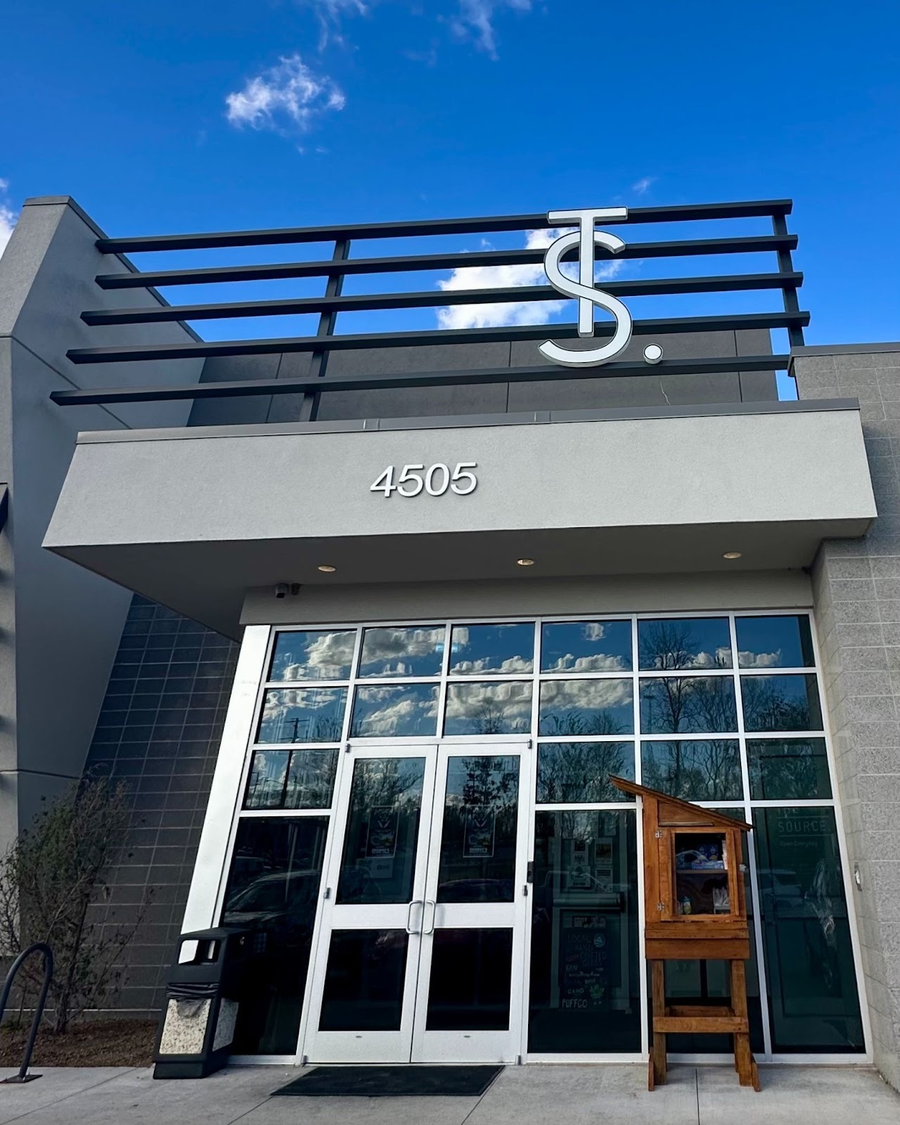 The Source dispensary storefront at 4505 W Poplar St in Rogers, Arkansas with wooden Sharing Shack community pantry near front entrance.