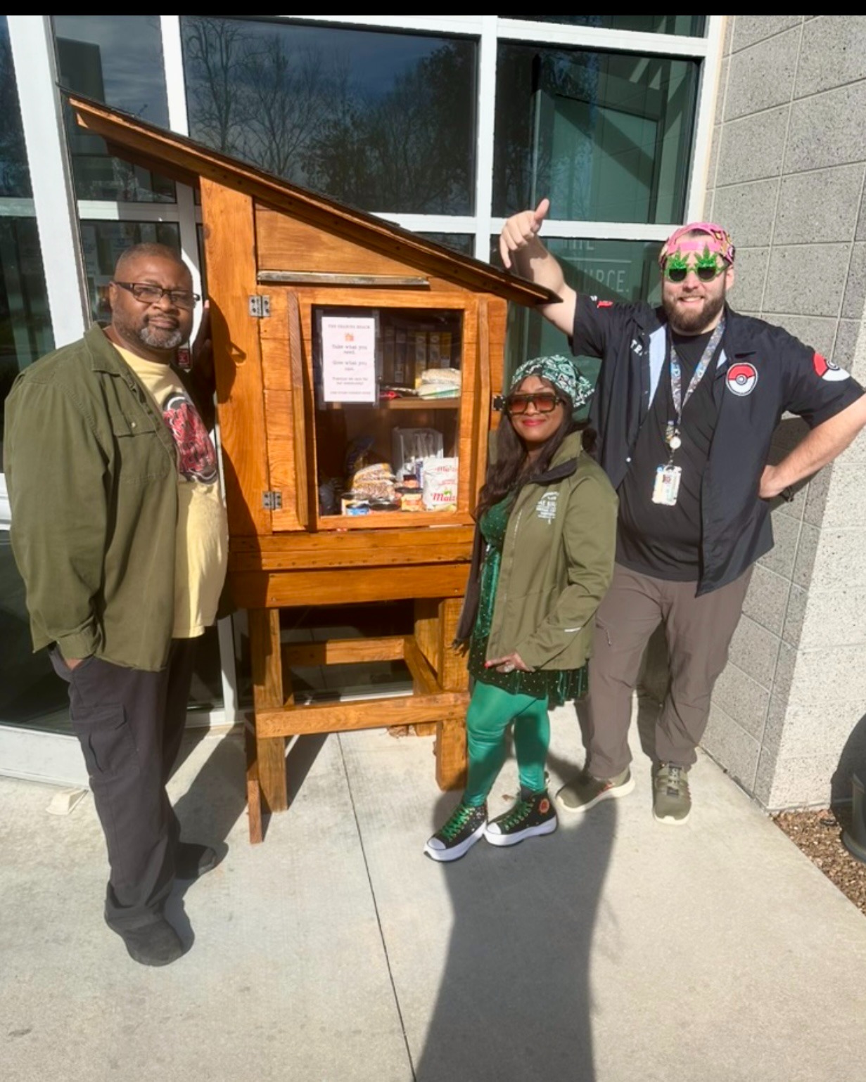 Two Source dispensary team members posing with Nate Walls and the Sharing Shack community pantry filled with donated items outside in Rogers, Arkansas.