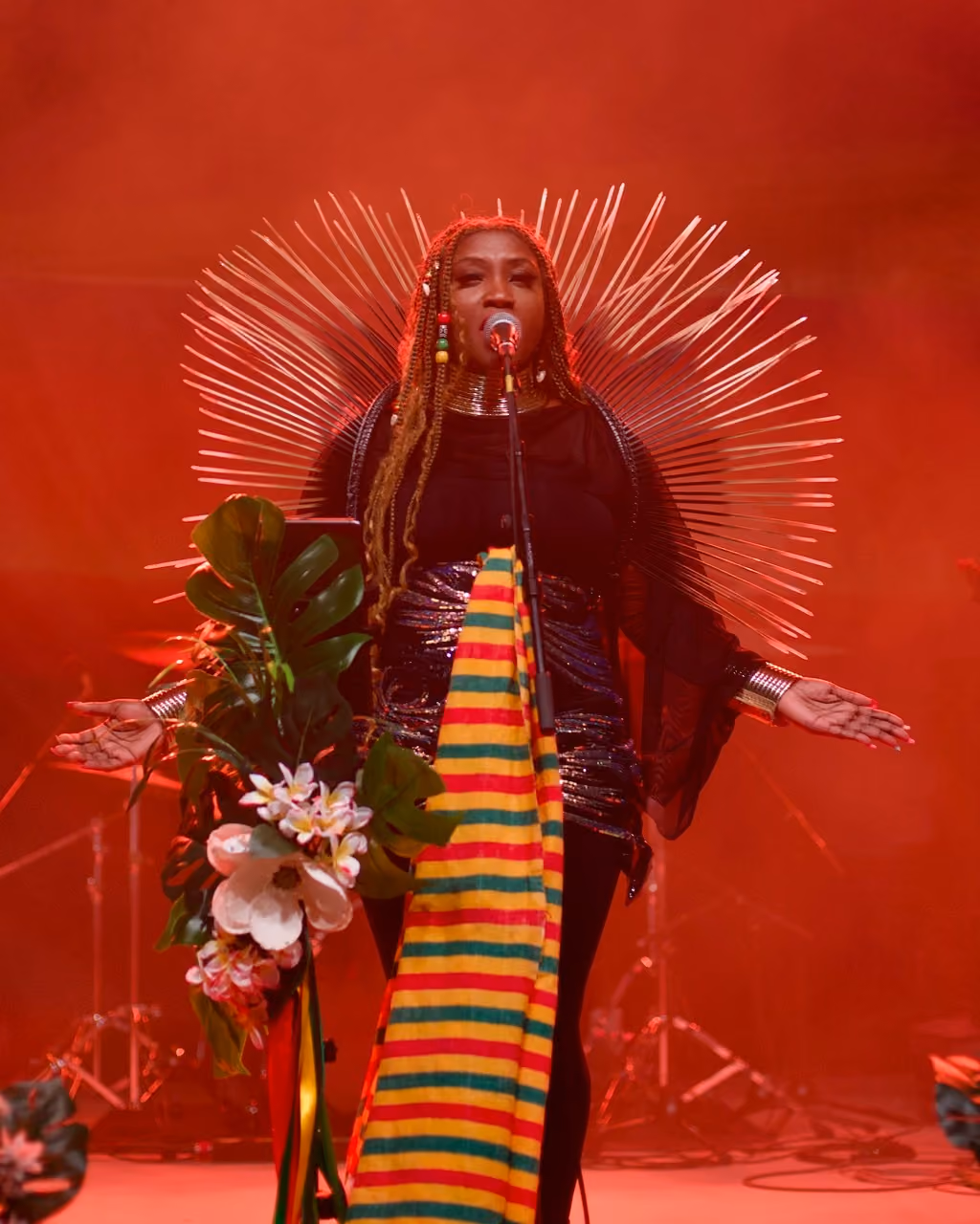Rochelle Bradshaw singing at The Source sponsored concert The Rail Yard in Rogers, Arkansas. Rochelle is wearing elaborate clothing and sings at a microphone covered in flowers.