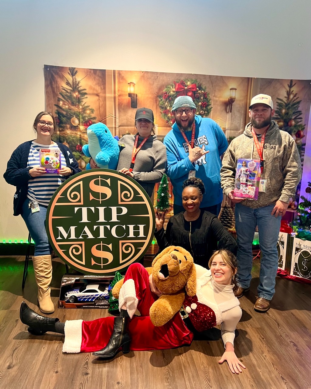 The Source team posing with Tip Match sign and donated toys at holiday nonprofit fundraiser event.