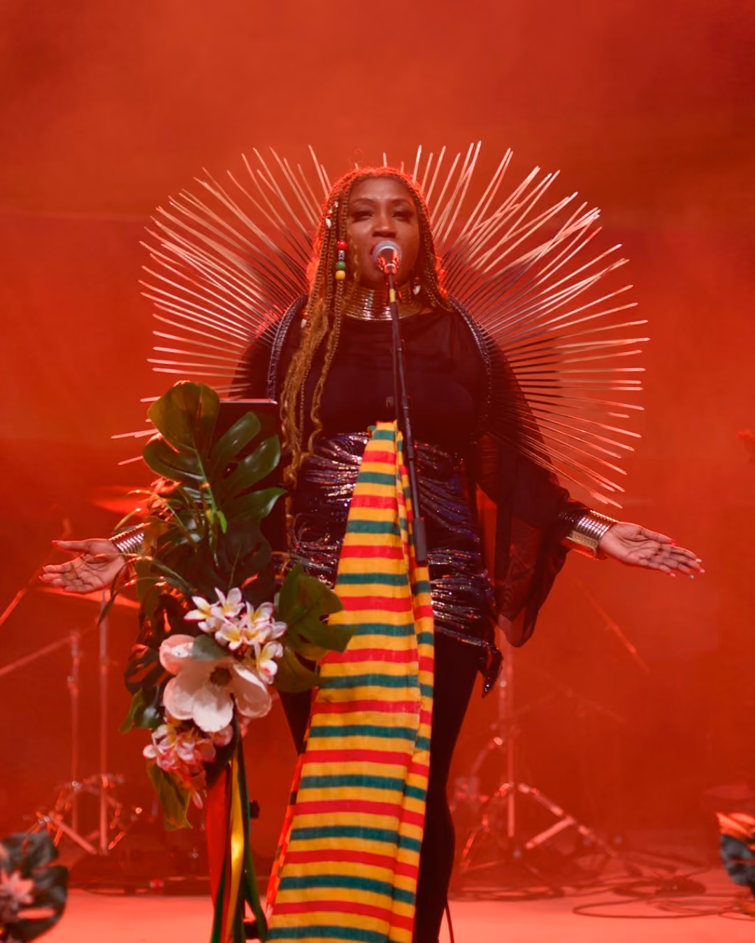 Rochelle Bradshaw performing on stage in a dramatic starburst headdress and Rastafarian-colored kente cloth, representing Northwest Arkansas cannabis culture at a reggae festival.