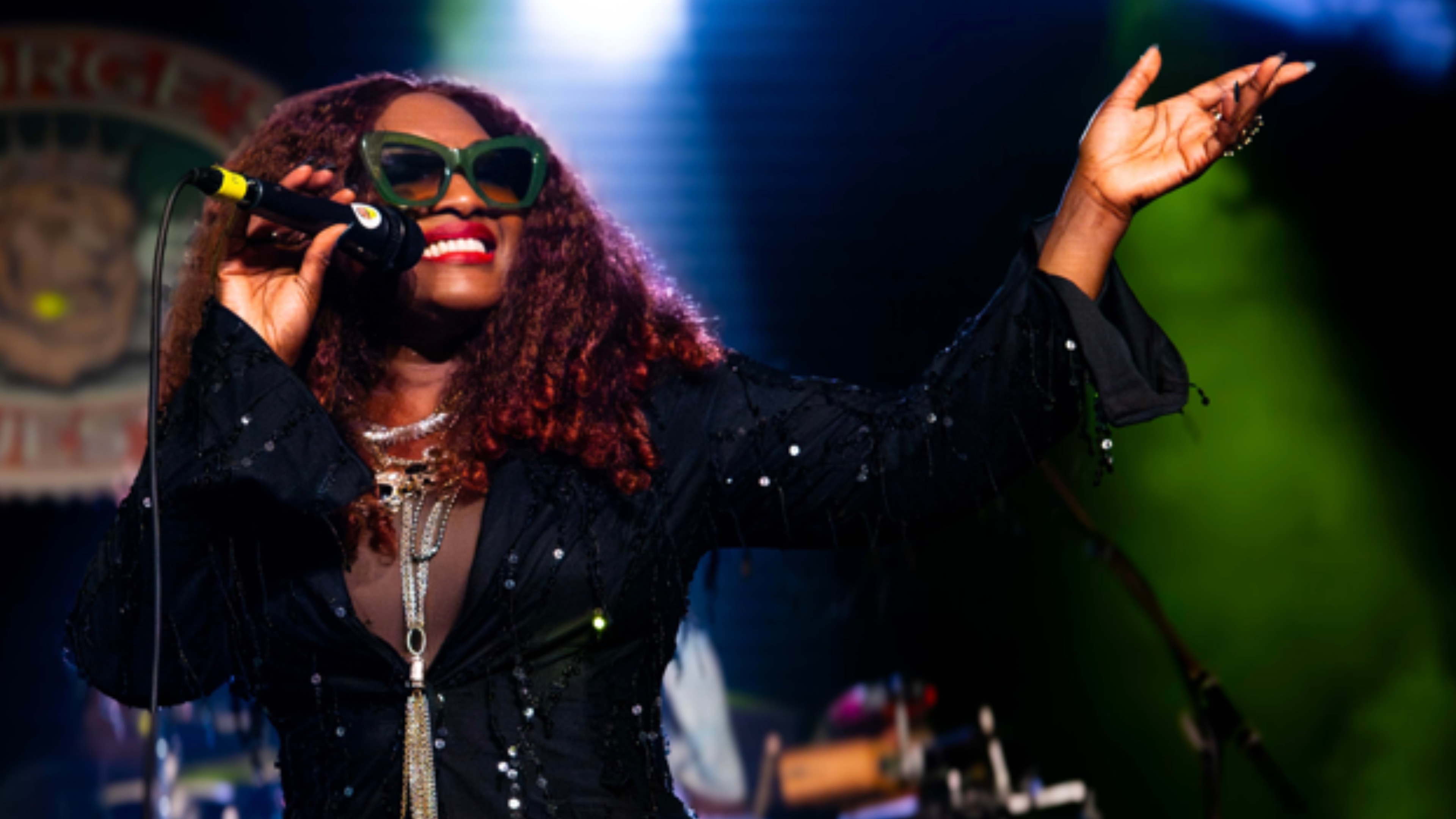 Rochelle Bradshaw performing a live reggae concert with microphone and sunglasses at Northwest Arkansas music venue.