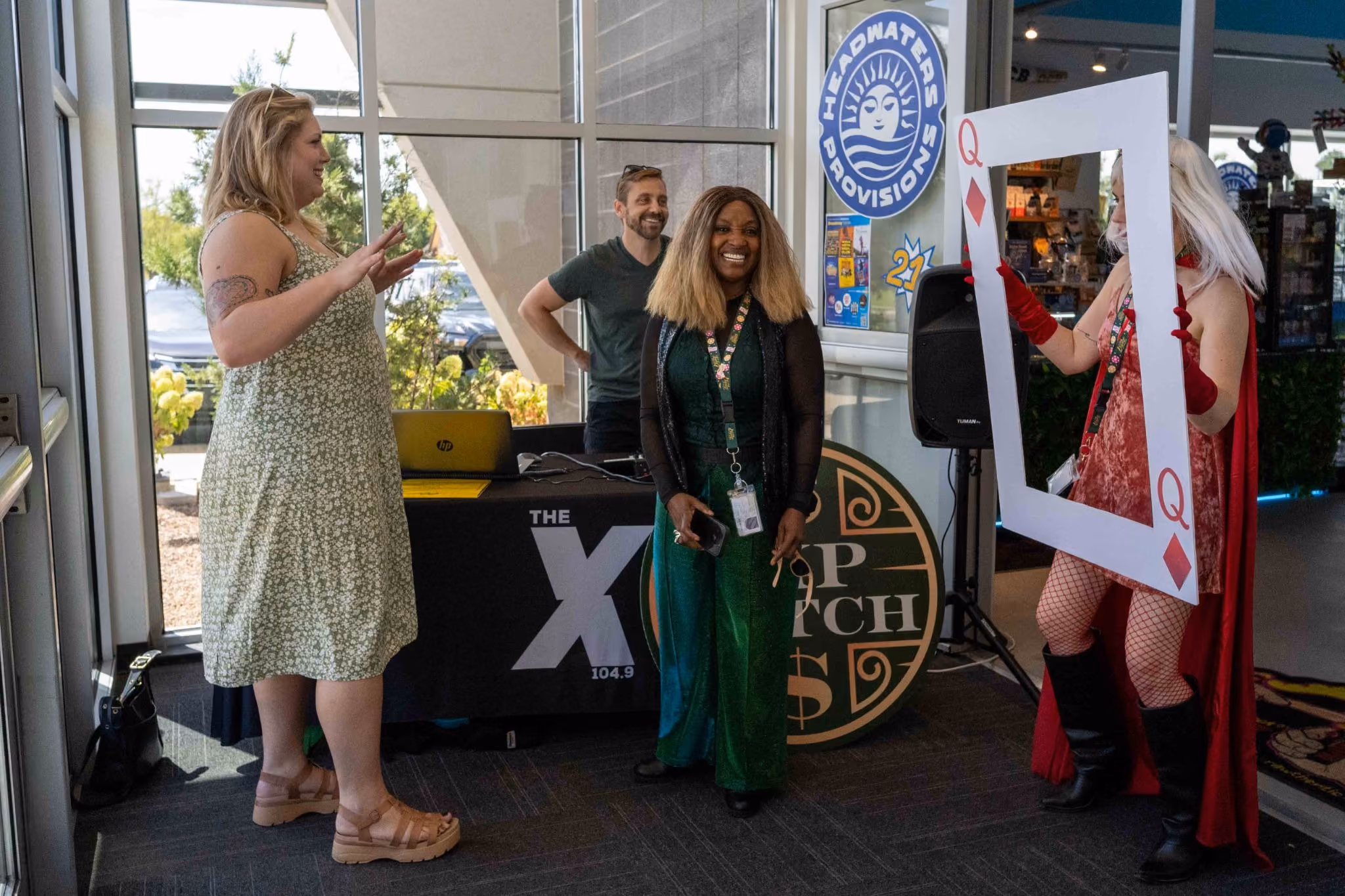104.9 the X broadcasts live from The Source's Lucky 7 Anniversary, with staff posing at the Headwaters Provisions table and a Queen of Diamonds photo prop.