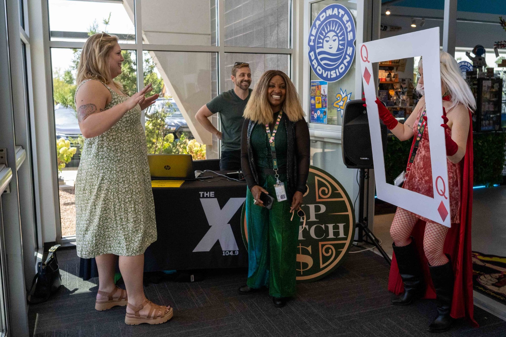 104.9 the X broadcasts live from The Source's Lucky 7 Anniversary, with staff posing at the Headwaters Provisions table and a Queen of Diamonds photo prop.
