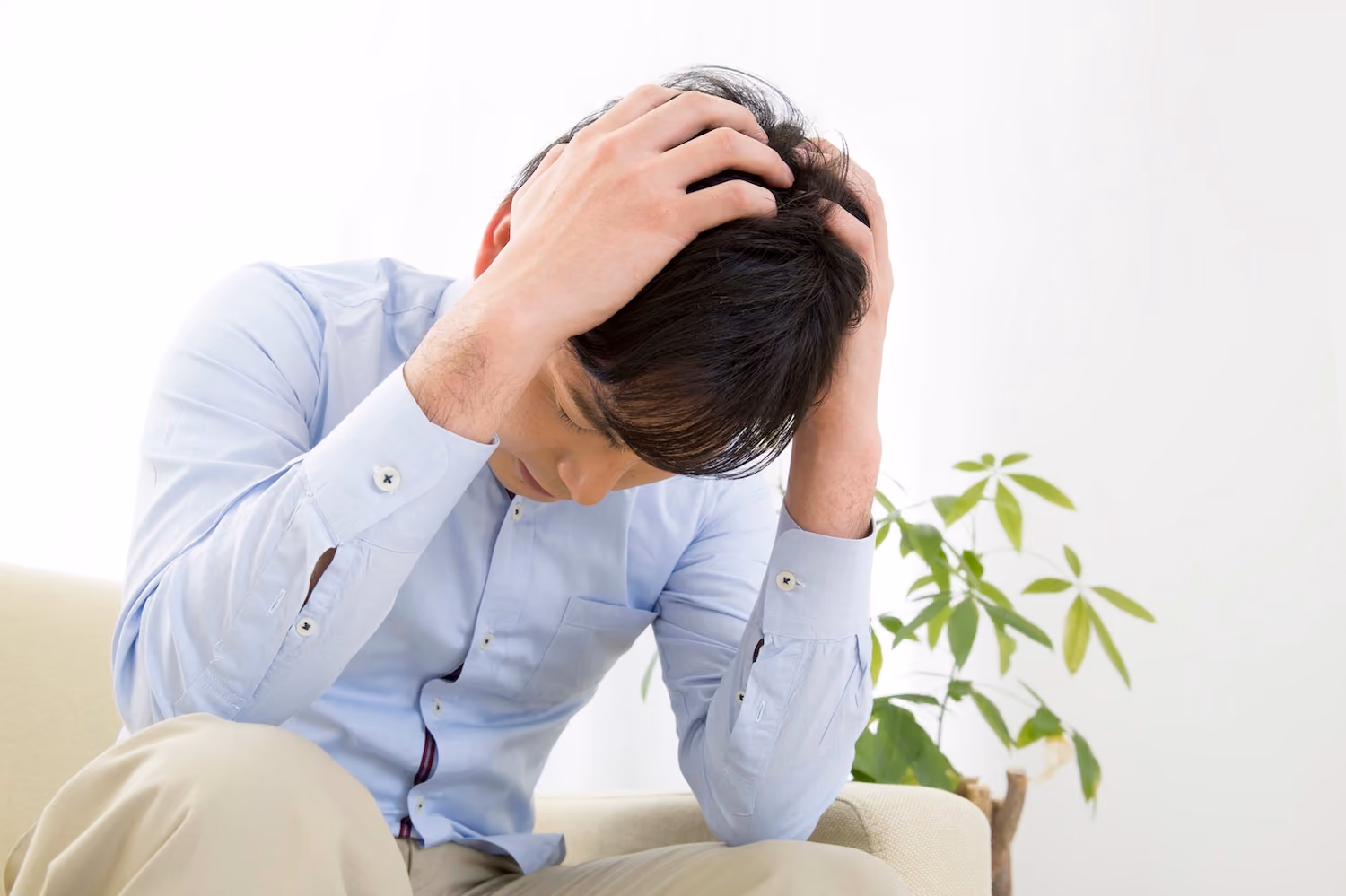 ソファで頭を抱えるEDに悩む男性