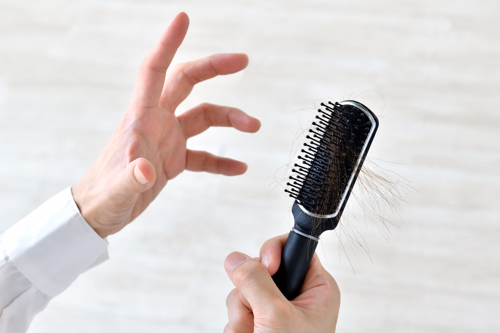ブラシについた自分の抜け毛をみて驚く男性の手