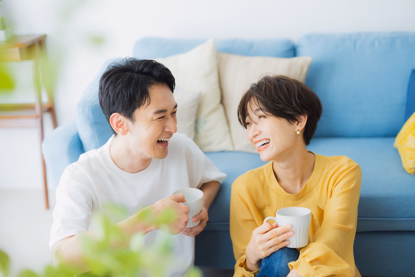 ソファの前に座りマグカップを手に微笑み合うカップル