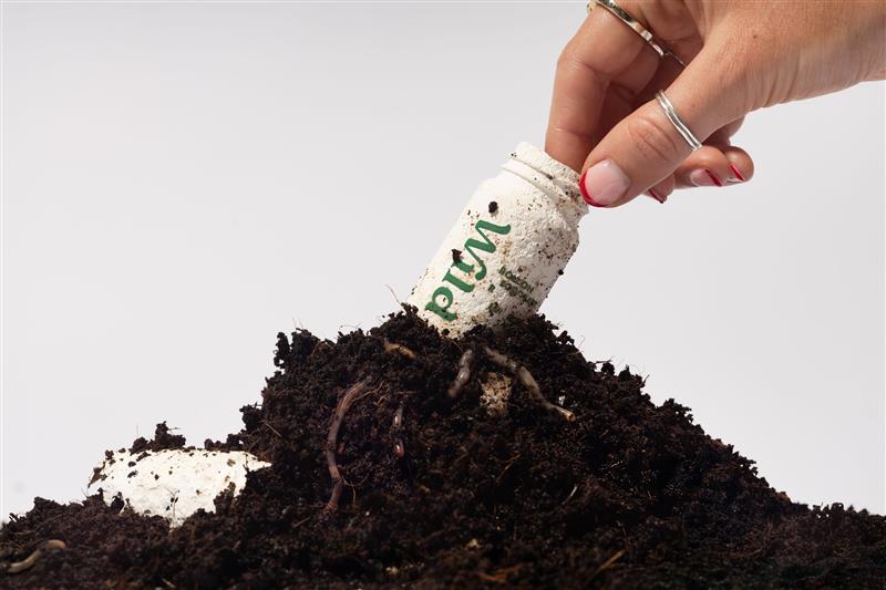 a compostable Wild brand packaging being taken from a fresh pile of soil by a hand