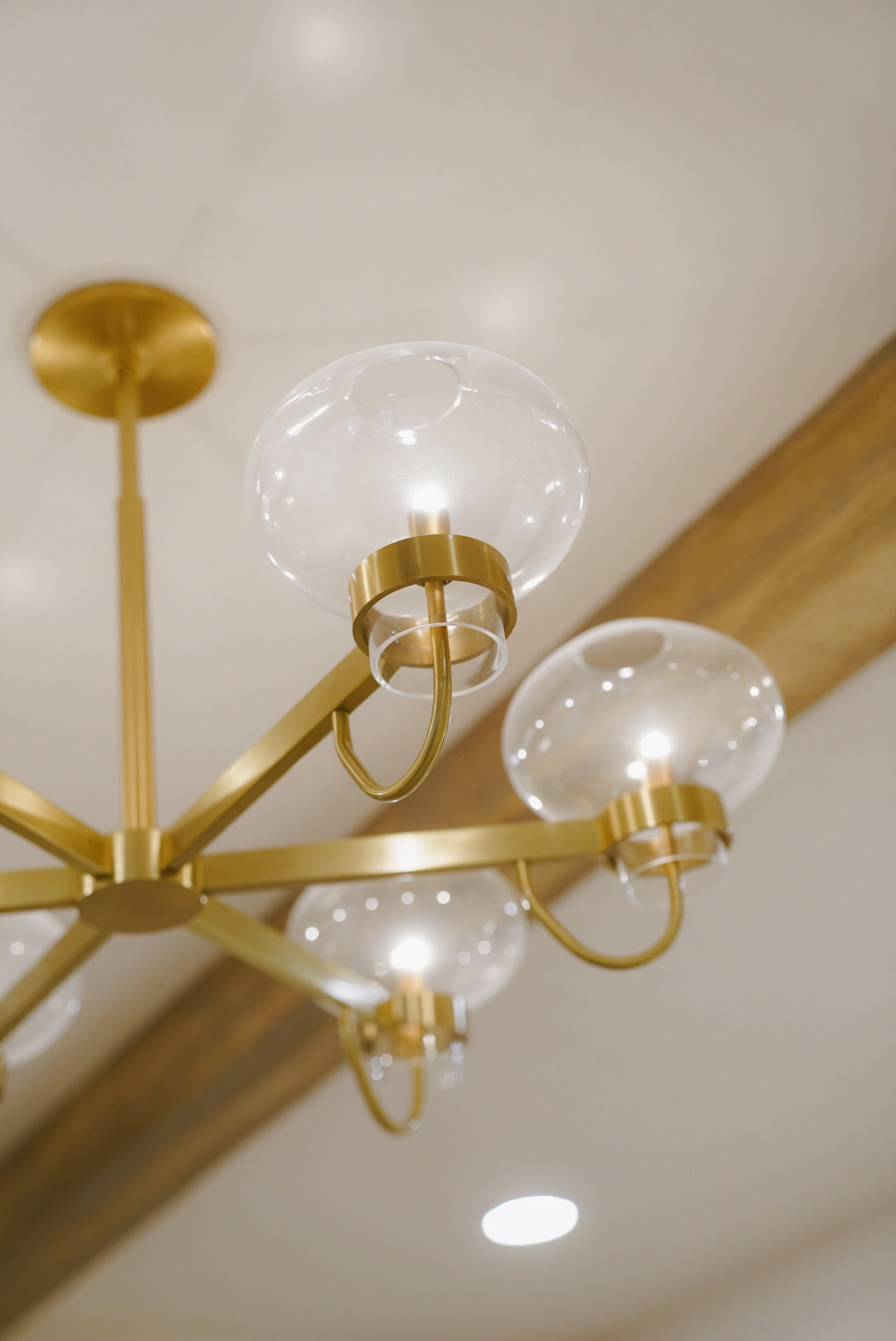 Modern chandelier with gold arms and clear glass globe light fixtures on a ceiling with wooden beams.