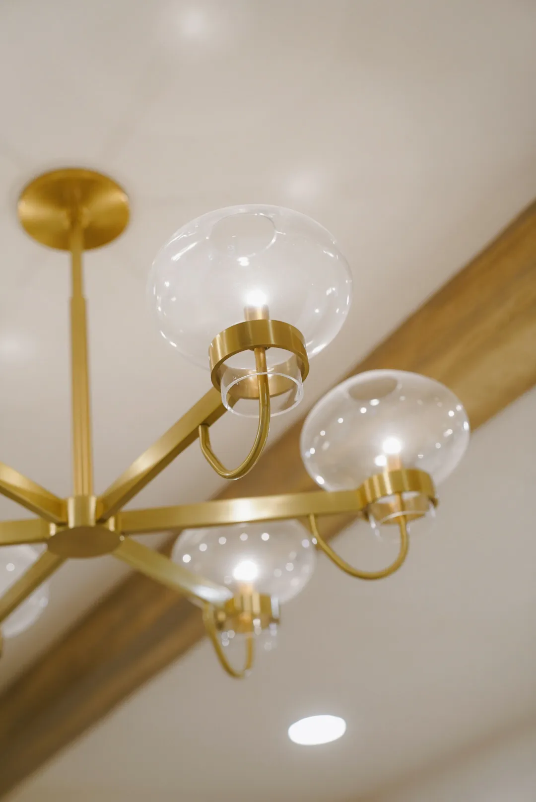 Modern chandelier with gold arms and clear glass globe light fixtures on a ceiling with wooden beams.