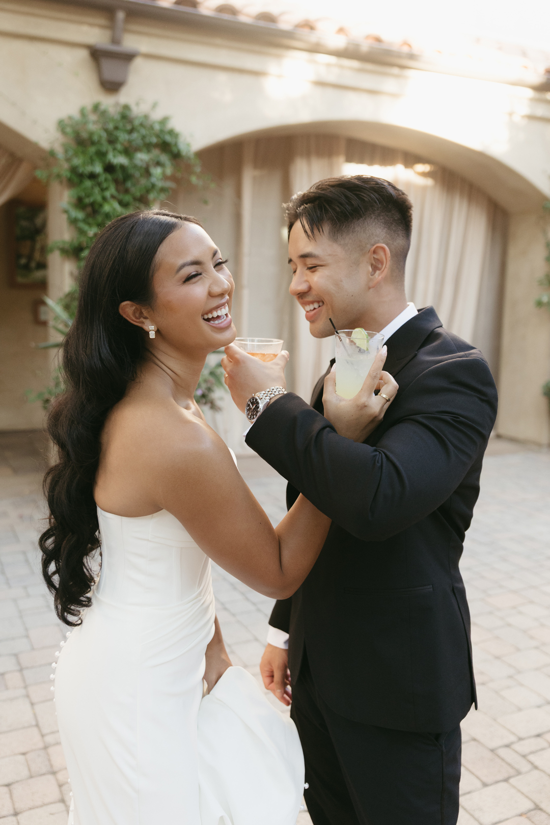 Bride and groom laugh while holding signature cocktails.