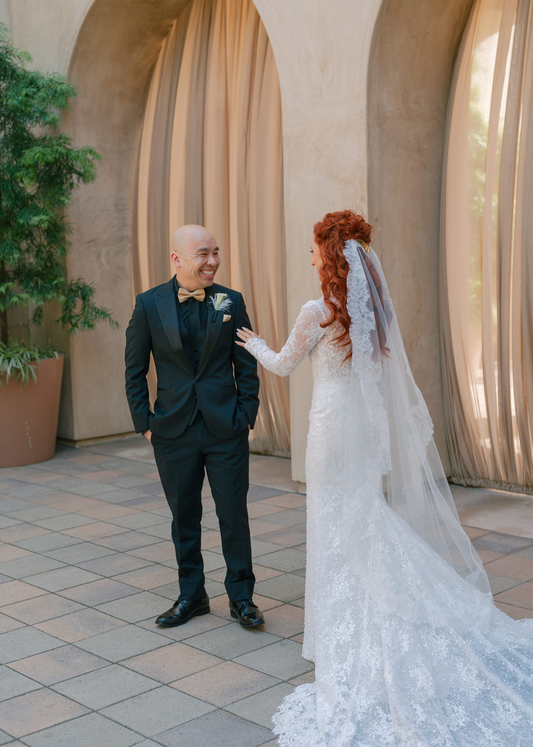 Bride and groom share first look at Serra Plaza wedding venue with sand colored draped archways as their backdrop.