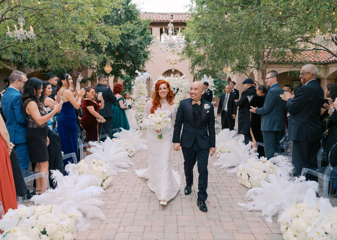 Bride and groom exit the cemeony as guests clap from both sides of the aisle.