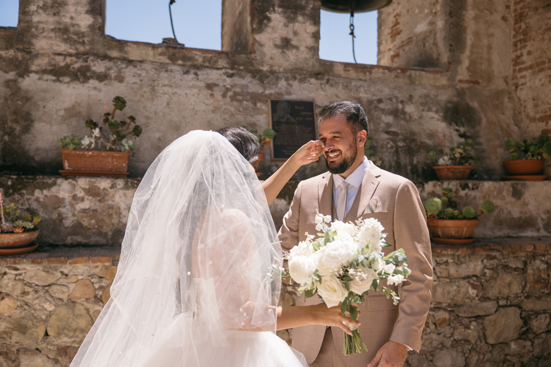 Bride brushes tear from Groom's face during first look at Mission San Juan Capistrano.