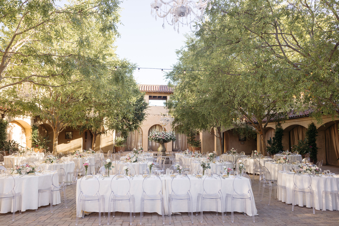 Blush flowers and eucalyptus decorate reception tables for an outdoor wedding reception in San Juan Capistrano.
