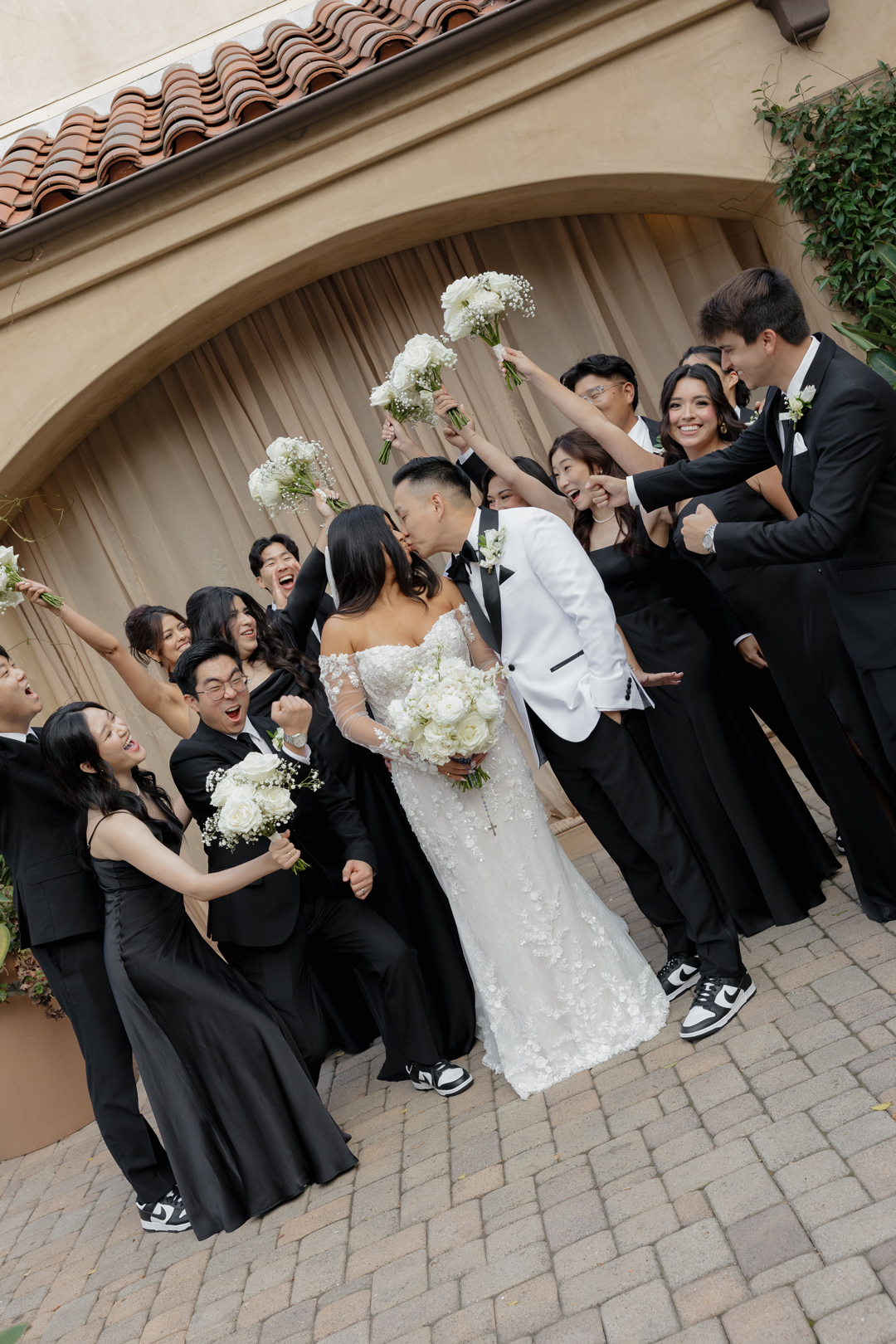Bridesmaids and groomsmen cheer as the bride and groom share a kiss in the middle of the friend group.