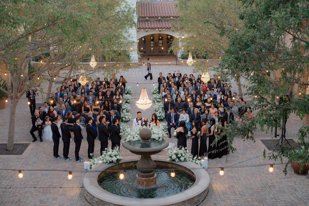 Bird's-eye-view of bride and groom together at the head of the aisle as guests watch.
