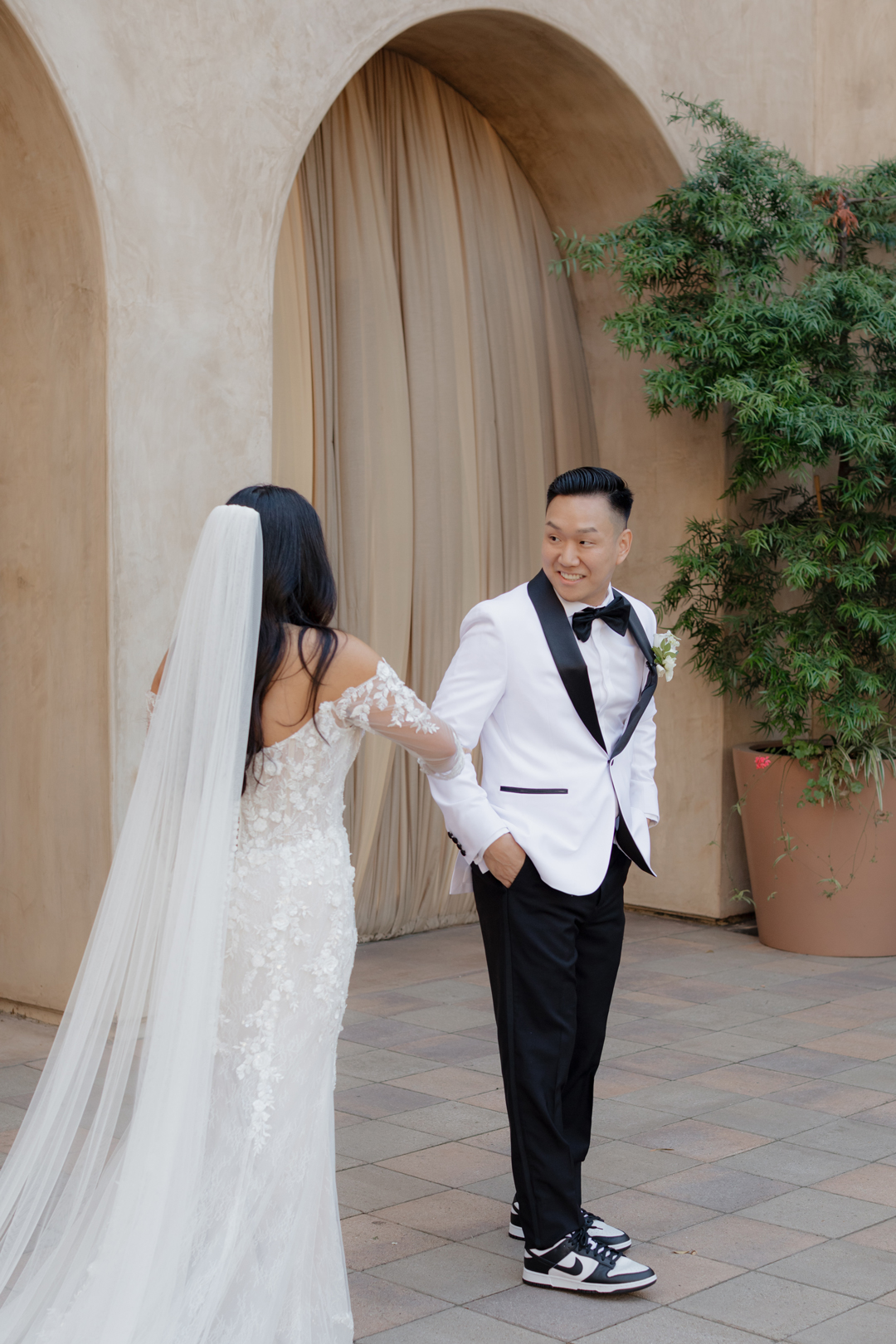 Groom happily sees bride for their first look in the Serra Plaza Courtyard with taupe draped loggias as the backdrop.