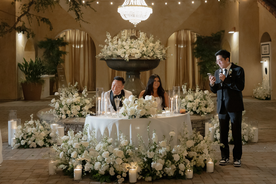 Friend shares a toast as the happy couple laughs from their sweetheart table.