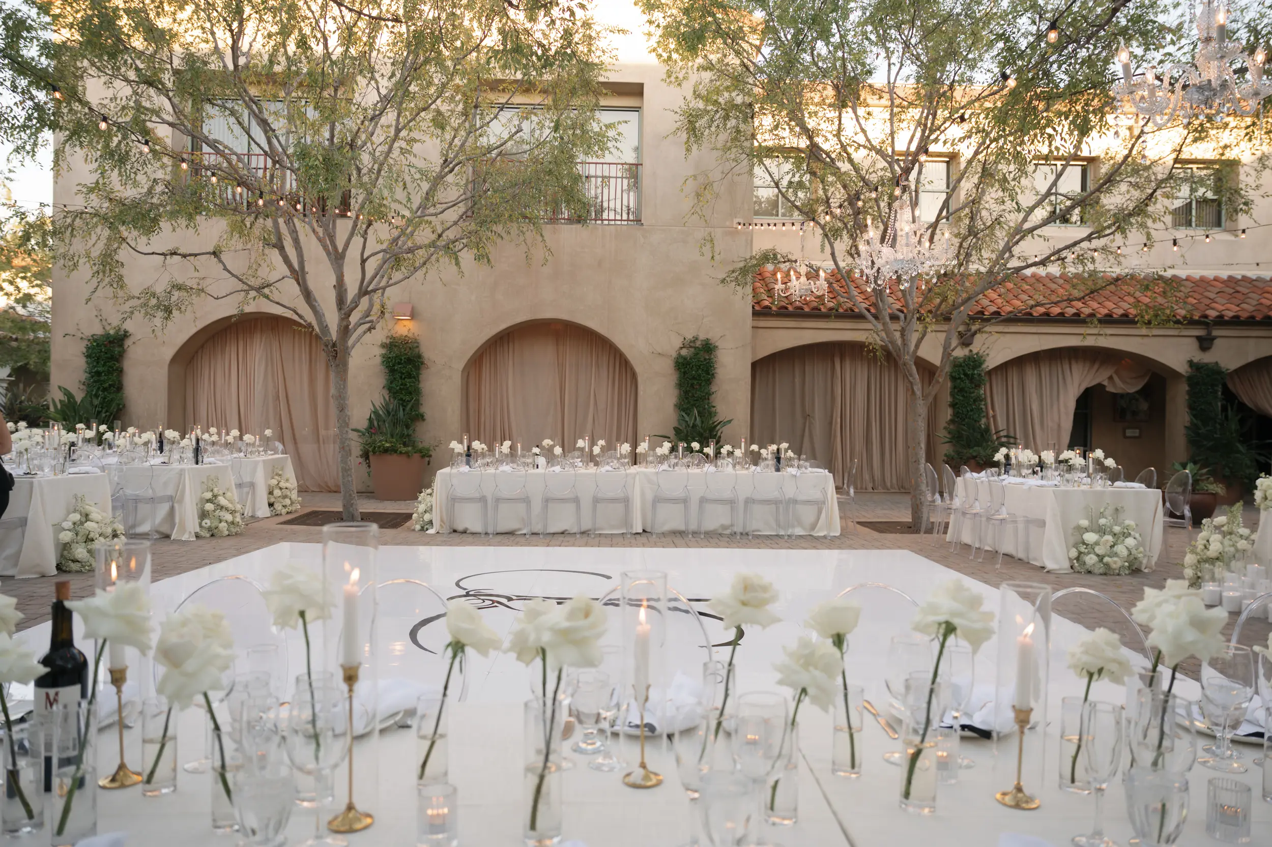 white roses are arranged in bud vases atop reception tables in the Serra Plaza Courtyard for the wedding reception.