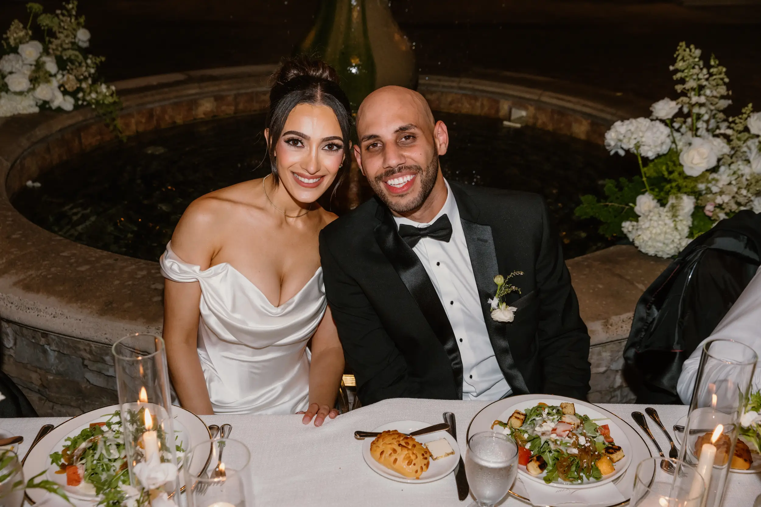 Bride and groom smile for the camera while sitting at their head table.