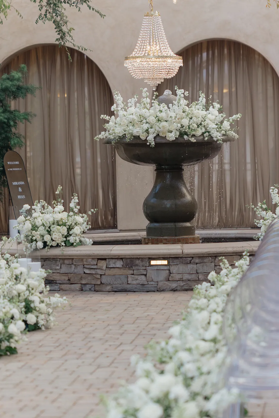 Spaninsh style wedding venue showcasing white flowers decorating the courtyard Spanish fountain and draped archway backdrop.