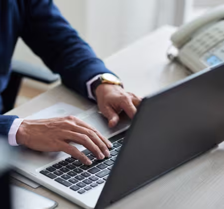 Close-up of male hands typing on a laptop computer with a landline phone in the background