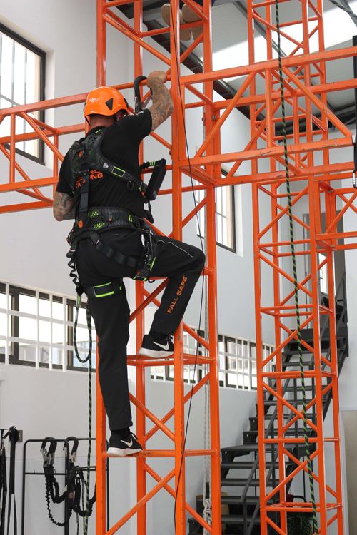 Person i Fall Safe fallskyddsutrustning klättrar i ställning
