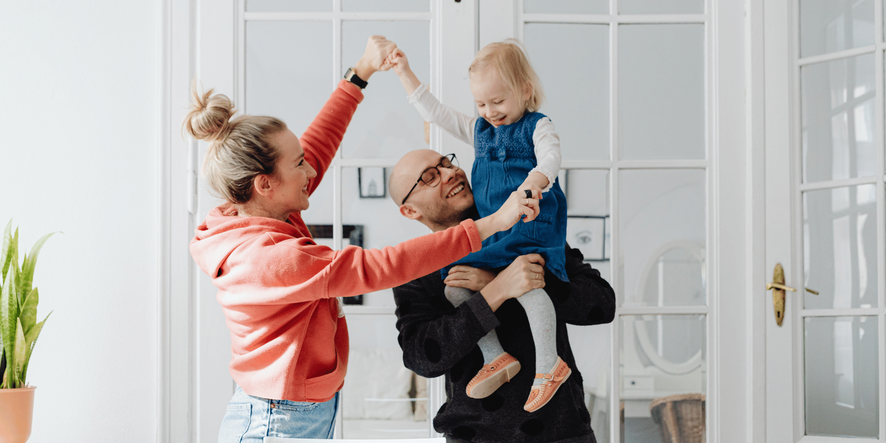 Eltern spielen fröhlich mit ihrer kleinen Tochter im hellen Wohnzimmer.